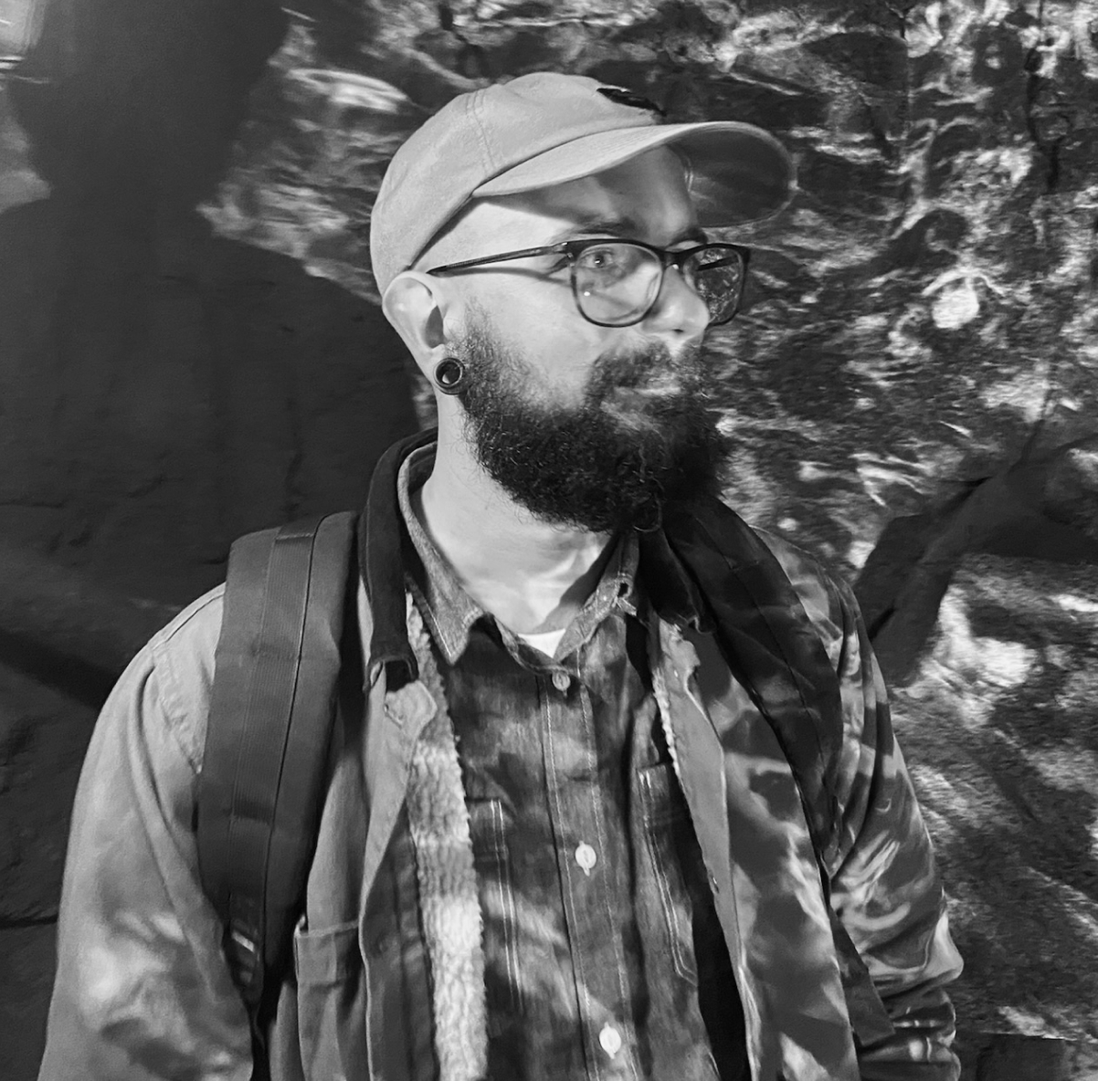 A picture of a dashing young man with glasses, a cap and a beard.